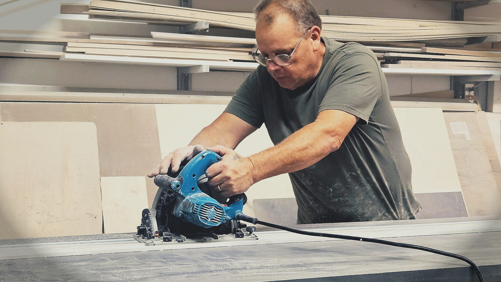 Solid surface fabricator cutting countertop slab with a track saw in professional workshop.